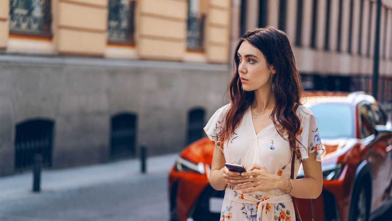 Eine Frau mit einem Smartphone steht vor einem Lexus Wagen