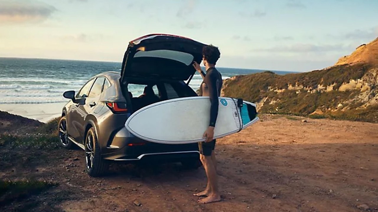 Mann mit Surfbrett an geöffneter Heckklappe eines Lexus NX