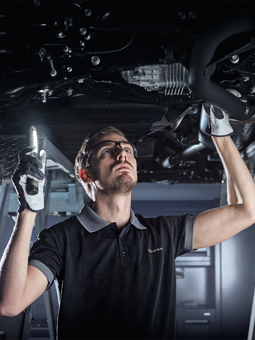 Ein Automechaniker kontrolliert ein Auto von unten mit einer Taschenlampe