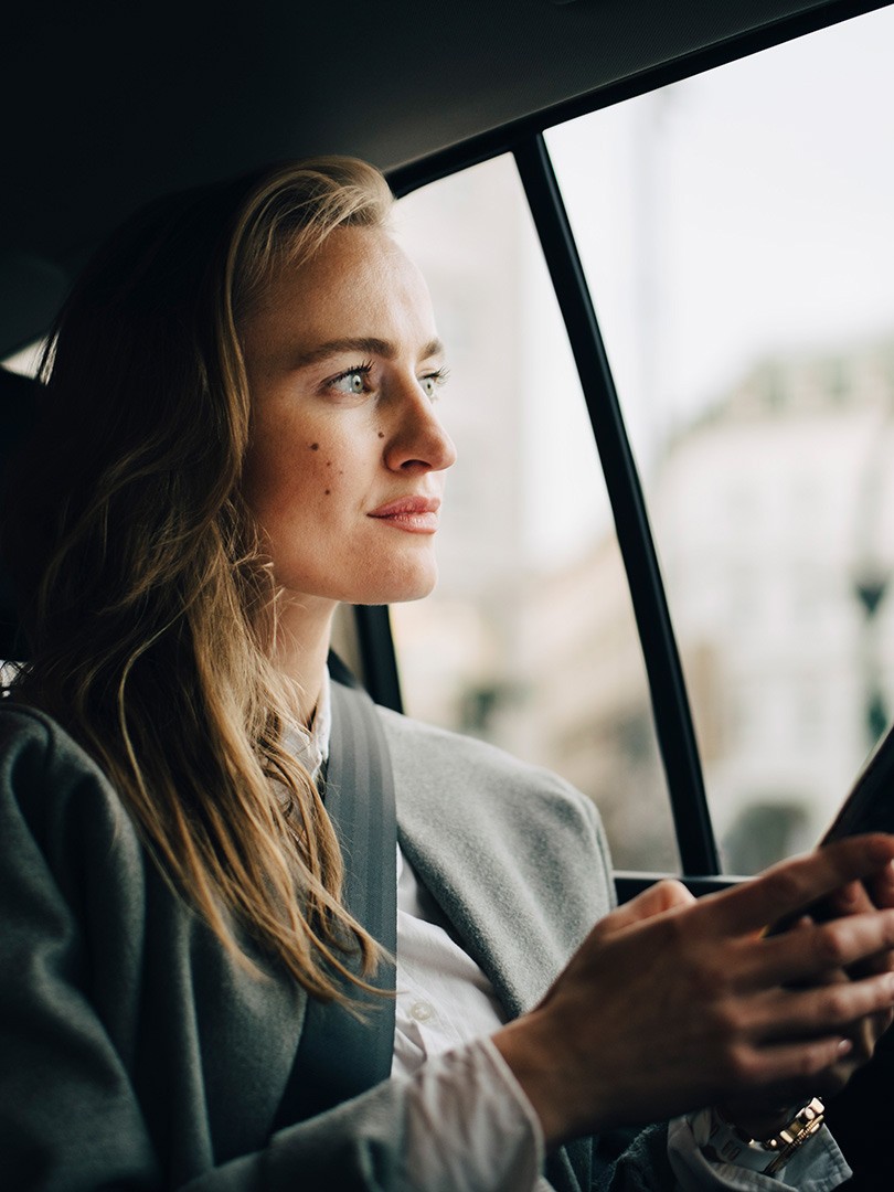 Junge Frau sitzt angeschnallt im Auto mit Smartphone in der hand