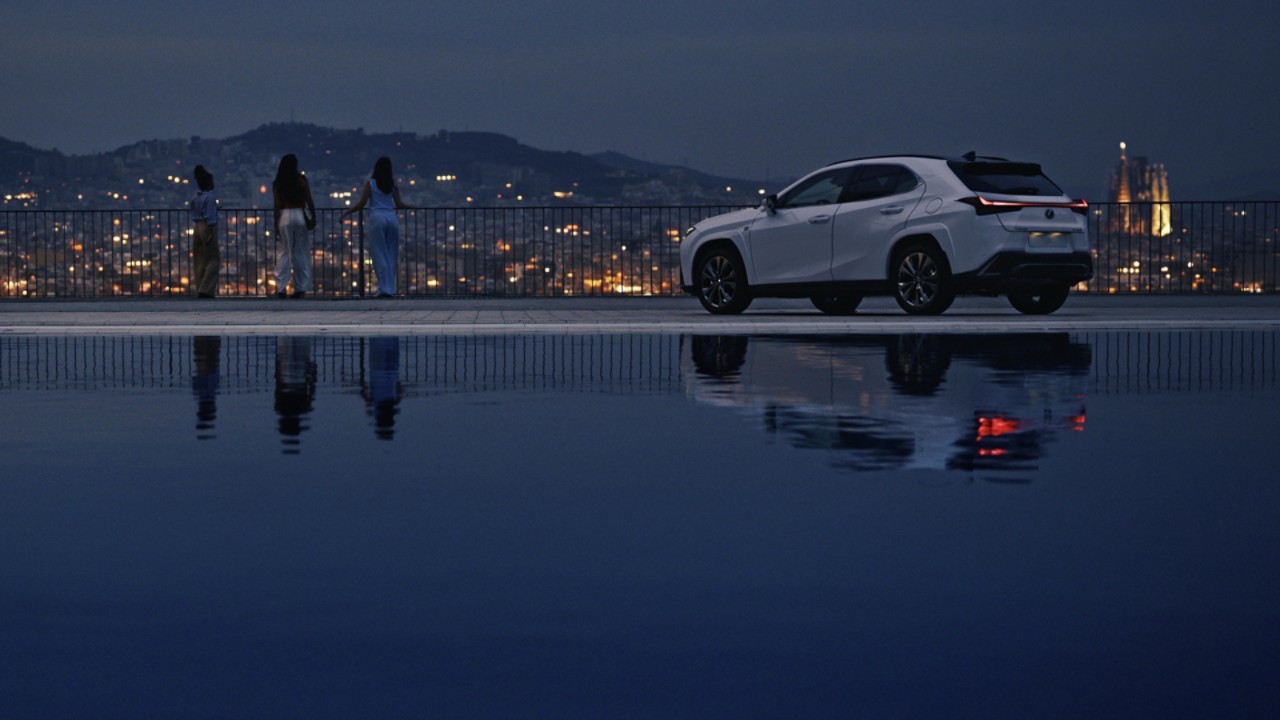 Drei Freundinnen neben Lexus UX 250h am Abend vor Stadt-Panorama am Meer