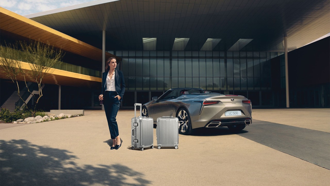Frau mit Rimowa Kofferset vor Lexus LC Cabriolet