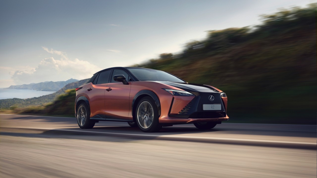 Lexus RZ in Kupferrot auf der Fahrt durch eine Landschaft